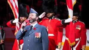 An RCAF member singing into a microphone in front of a Colour Guard.